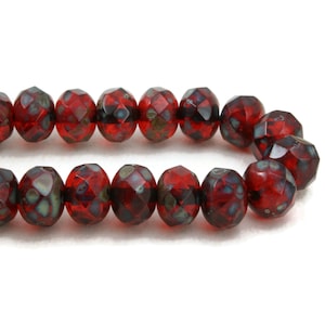 May include: Strand of faceted red glass beads with a mottled, dark blue-green pattern. The beads have an oval shape and are strung together, ideal for jewelry making or crafting projects.