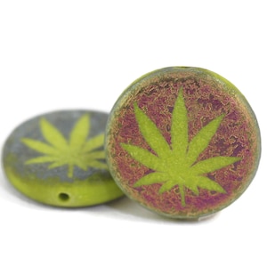 May include: Two round green ceramic beads with a green marijuana leaf design. The beads have a textured surface and a hole in the center.