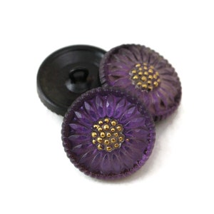 May include: Two purple glass buttons with a raised flower design and gold accents.