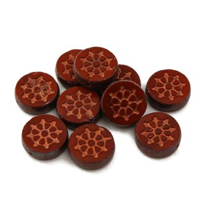 May include: A group of ten brown ceramic round tiles with a raised design of a stylized flower in the center.