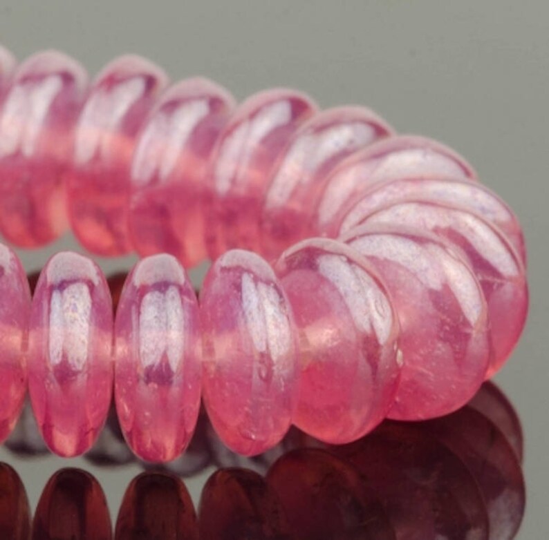 May include: A close-up of a pink hair scrunchie made of small, round beads. The beads have a slight iridescent sheen.