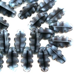 May include: A collection of leaf-shaped beads in shades of gray and white. The beads have a textured, ridged design and are arranged against a white background. These beads are suitable for jewelry making and craft projects.