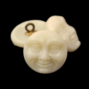 May include: Three white ceramic buttons with a smiling face design. The buttons have a gold metal shank.