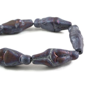 May include: A strand of dark gray glass beads with a textured, iridescent finish. Each bead is shaped like a small human figure.