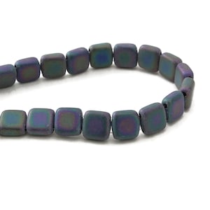 May include: A string of iridescent square beads. The beads have a matte finish and shift in colour from green to purple and blue. The beads are strung together, creating a curved line against a white background. Suitable for jewellery making.