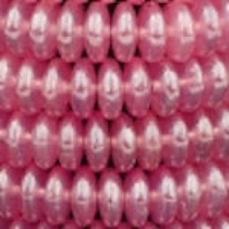 May include: A strand of pink pearl-like beads. The beads are oval shaped and have a smooth, glossy finish.