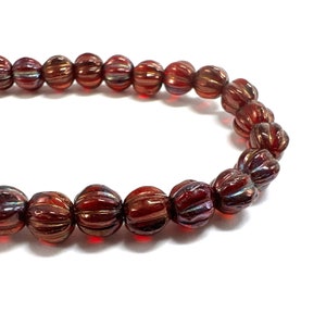 Può includere: Una collana di perline di vetro rosso con una texture a coste e una finitura iridescente.