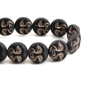 May include: A strand of black beads with a decorative design in a metallic gold color. The beads are round and have a slightly textured surface.