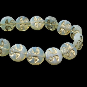 May include: A strand of opalescent glass beads with gold-colored, stylized designs. The beads are round and have a slightly irregular shape. The background is solid black, highlighting the beads' details.