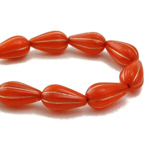 Peut inclure: Un brin de perles de verre orange avec des accents dorés. Les perles sont en forme de goutte et ont une surface texturée.