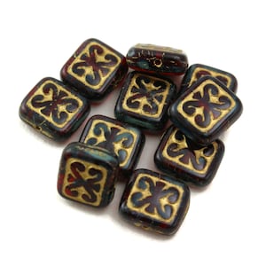 May include: A pile of dark red glass square beads with gold accents. Each bead has a decorative design in the center.