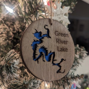May include: A wooden Christmas ornament with a blue outline of Green River Lake. The ornament is hanging on a Christmas tree.