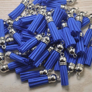 Puede incluir: Un conjunto de borlas azul real con tapas y lazos de metal plateado. Las borlas están hechas de un material suave y deshilachado. Las tapas plateadas tienen un acabado redondeado y pulido. Estas pequeñas borlas son ideales para la fabricación de joyas o proyectos de artesanía.