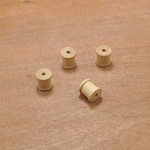 Puede incluir: Cuatro carretes de madera, cada uno con un agujero en el centro, están dispuestos sobre una superficie de madera marrón claro.