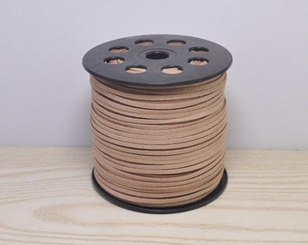 May include: A spool of tan-colored, flat leather cord. The cord is neatly wound around a black plastic spool with multiple holes. The cord appears to be made of suede or a similar material, and is ready for crafting projects.