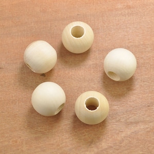 Könnte beinhalten: Fünf unfertige Holzperlen auf einer hellbraunen Oberfläche. Jede Perle ist kugelförmig und hat eine natürliche Holzfarbe. Einige Perlen haben ein Loch, andere ein kleineres Loch an der Seite.