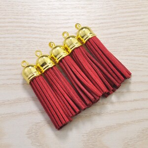 Könnte beinhalten: Fünf rote Quasten-Schlüsselanhänger mit goldenen Metallkappen. Die Quasten bestehen aus einem weichen, flauschigen Material.