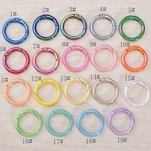 May include: A collection of nineteen colorful metal spring gate rings in various shades, including blue, green, pink, and yellow. Each ring is numbered from 1 to 19, with a hinged opening for attaching to other items.