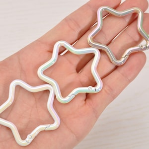 May include: Three iridescent star-shaped clasps. The clasps are made of metal and have a pearlescent finish that reflects a rainbow of colors. Each clasp has a hinged opening for attaching to other items.