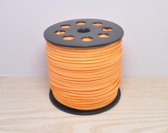 May include: A spool of orange suede cord wrapped around a black plastic bobbin. The cord is approximately 3 mm wide.
