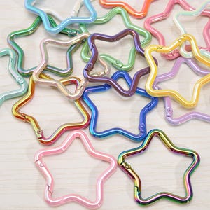 May include: A collection of star-shaped metal clasps in various colors, including pink, blue, green, and iridescent finishes. These clasps are designed for use in crafting or jewelry making.