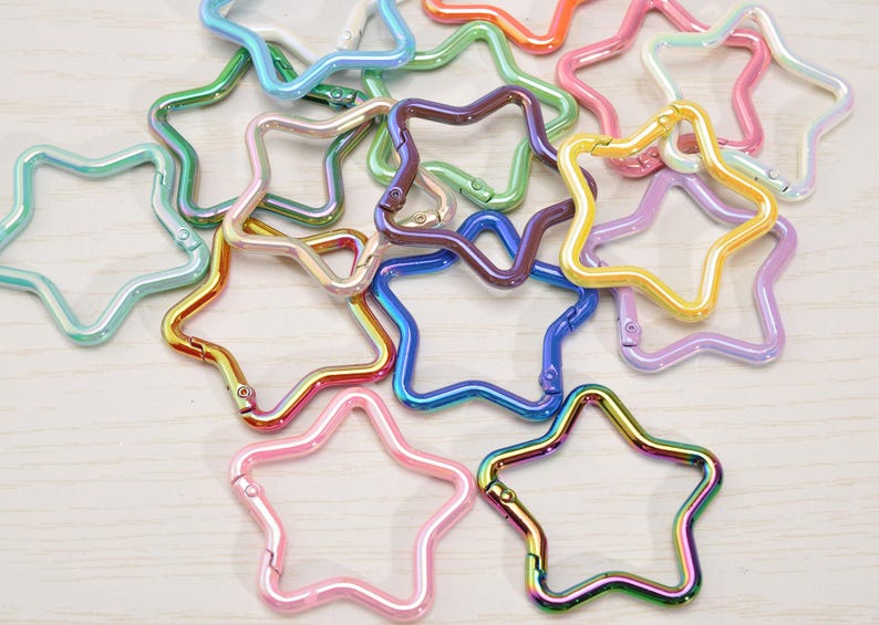 May include: A collection of star-shaped metal clasps in various colors, including pink, blue, green, and iridescent finishes. These clasps are designed for use in crafting or jewelry making.