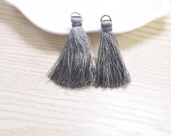 May include: Two gray tassel earrings with gold-colored hoops. The tassels are made of silky threads, and the top of each tassel is wrapped in a darker gray thread. The earrings are displayed on a white surface.