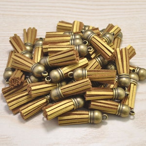 Könnte beinhalten: Ein Haufen goldener Lederquasten mit antiken Messingkappen. Die Quasten sind etwa 2,5 cm lang und haben eine fransige Textur.
