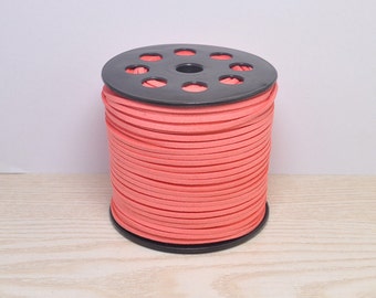 May include: A spool of coral pink suede cord wrapped around a black plastic spool with holes.