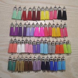 Puede incluir: Una colección de 28 borlas coloridas con tapas plateadas. Las borlas están dispuestas en filas y presentan una variedad de colores, incluyendo verde, rojo, amarillo, rosa, morado y azul. Cada borla está numerada del 1 al 28.