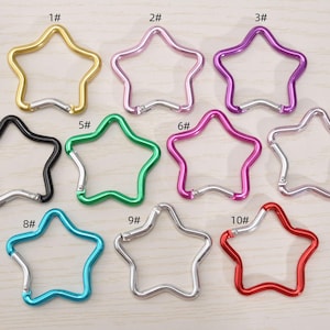 Puede incluir: Una colección de diez mosquetones en forma de estrella en varios colores, incluyendo dorado, rosa, morado, negro, verde, plateado, turquesa y rojo. Cada clip tiene un cierre plateado. Estos clips son adecuados para llaveros o bolsos.
