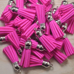 Könnte beinhalten: Ein Haufen leuchtend pinkfarbener, flauschiger Quasten mit silbernen Metallspitzen. Die Quasten sind in einem zufälligen Muster angeordnet und alle gleich groß.