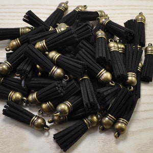 Puede incluir: Un montón de borlas de ante negro con tapas de metal dorado antiguo. Las borlas miden aproximadamente 5 cm de largo.