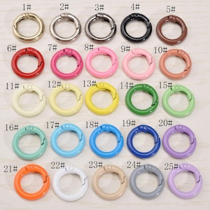 Può includere: Una collezione di 25 anelli a scatto a molla in vari colori, tra cui oro, argento, nero, marrone, rosso, rosa, giallo, verde, blu, arancione, bianco, beige, grigio e viola. Ogni anello è numerato.