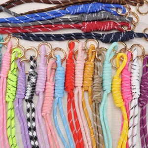May include: A selection of brightly coloured lanyards with gold key rings. The braided cords come in a variety of colours, such as white, pink, green, purple, blue, red, and black. Some have a striped design.
