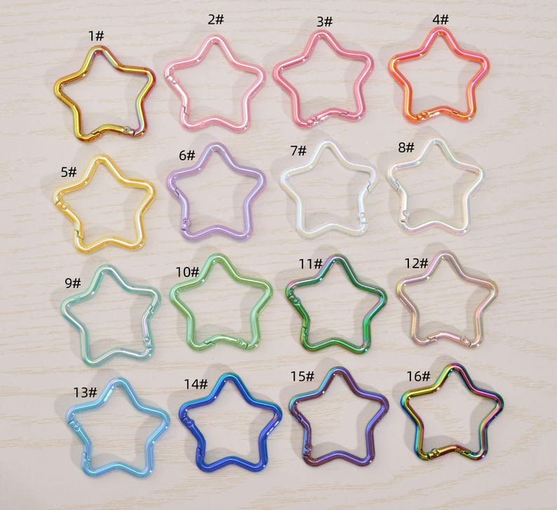 May include: A collection of sixteen star-shaped metal keychains in various colors, including gold, pink, purple, green, and blue. Each keychain has a clasp for attaching to keys or other items. The keychains are numbered 1 through 16.