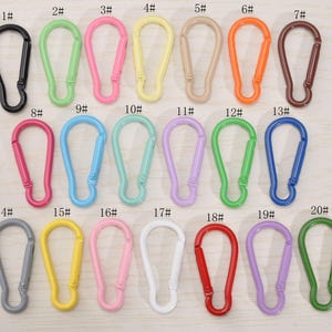 May include: A collection of twenty carabiner clips in various colors, including black, green, pink, yellow, tan, orange, brown, red, blue, and purple. Each clip has a spring-loaded gate for secure closure.