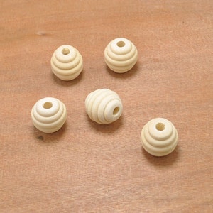 May include: Five unfinished wooden beads with a grooved, spherical design. Each bead has a central hole and a light, natural wood color. The beads are arranged on a light brown wooden surface.