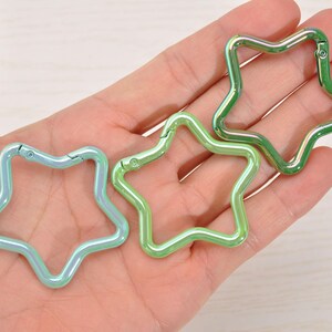 May include: Three star-shaped carabiner clips in iridescent green and blue hues. The clips are made of metal and have a spring-loaded gate for easy attachment. These decorative clips can be used for keychains, bag charms, or other craft projects.