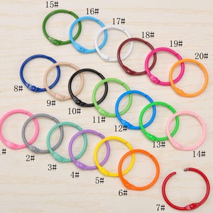 May include: A collection of twenty colorful metal loose-leaf binder rings arranged in a grid. Each ring features a hinged opening mechanism and is labeled with a corresponding number from 1# to 20# in black text, showcasing various hues.