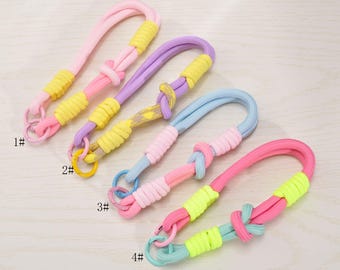 Pode incluir: Quatro chaveiros coloridos em rosa, roxo, azul e rosa com detalhes em amarelo. Cada chaveiro apresenta uma alça, um nó e um anel de metal. Os chaveiros são feitos de um material macio e tecido.