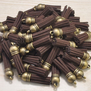 Könnte beinhalten: Ein Haufen brauner Wildleder-Quasten mit goldenen Metallkappen. Die Quasten sind etwa 2,5 cm lang.