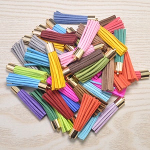 Könnte beinhalten: Eine Ansammlung bunter Quasten in verschiedenen Farbtönen, darunter Blau, Rosa, Gelb und Grün. Jede Quaste hat eine goldfarbene Metallkappe. Diese dekorativen Quasten eignen sich für die Schmuckherstellung, zum Basteln oder um Accessoires aufzupeppen.