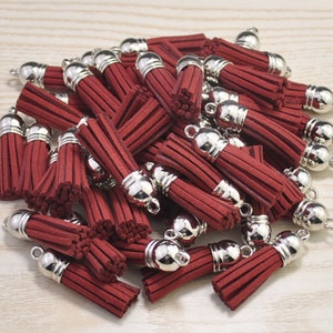 Könnte beinhalten: Ein Haufen roter Samtquasten mit silbernen Metallkappen. Die Quasten sind etwa 5 cm lang und perfekt, um jedem Projekt einen Hauch von Eleganz zu verleihen.