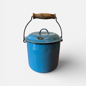 May include: A vintage blue enamelware pot with a lid and a wooden handle. The pot has a metal handle and a dark rim. The pot is a light blue color and is likely used for cooking or storage. The pot is a classic kitchenware item.