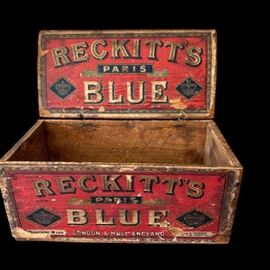 May include: An antique wooden box with a hinged lid, painted red with gold lettering. The box reads "RECKITT'S PARIS BLUE" and includes the text "LONDON & HULL ENGLAND". The box is open, revealing the wooden interior.