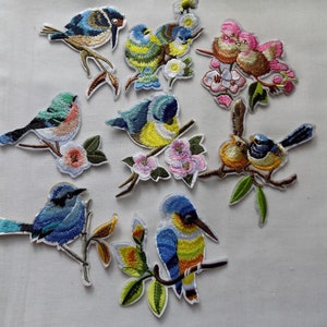 May include: A set of ten embroidered iron-on patches featuring colorful birds perched on branches with flowers. The birds are blue, green, yellow, and brown with white accents. The flowers are pink, white, and yellow.