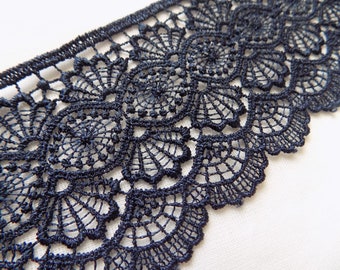 May include: A strip of dark navy blue lace trim featuring a repeating scalloped edge pattern with intricate circular and fan-shaped motifs. The lace has a dense, textured thread construction with a defined straight top border and a decorative curved bottom edge.