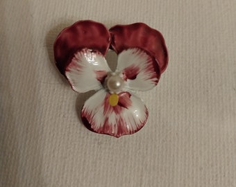 May include: A red and white enamel flower brooch with a pearl accent. The flower is a pansy with a yellow center.