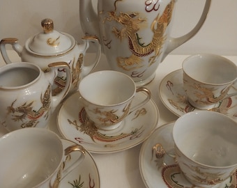 May include: A white porcelain tea set with a gold dragon design. The set includes a teapot, sugar bowl, creamer, and four teacups and saucers.